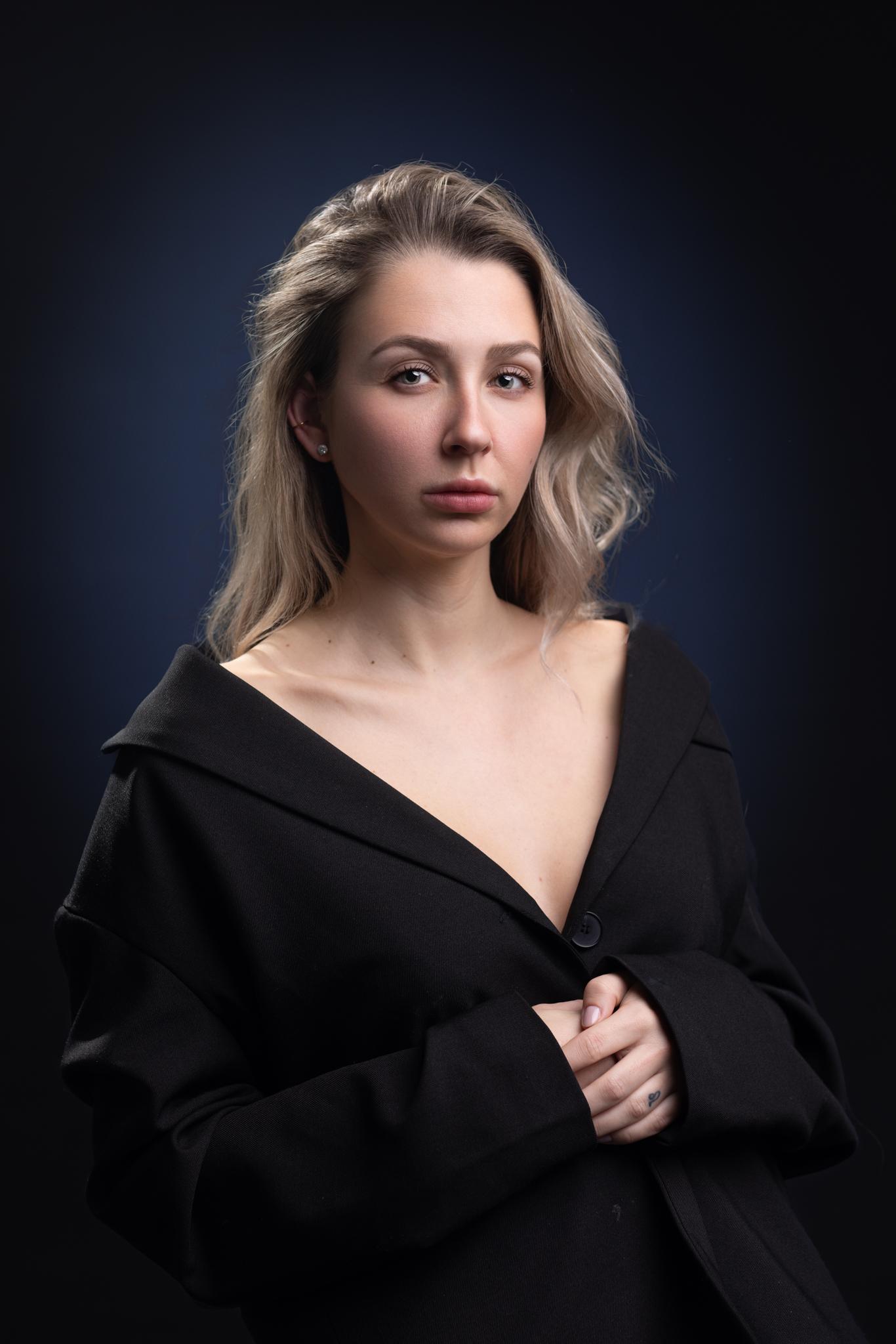 Portret van model Liz met open zwarte jas voor donkere blauwe achtergrond