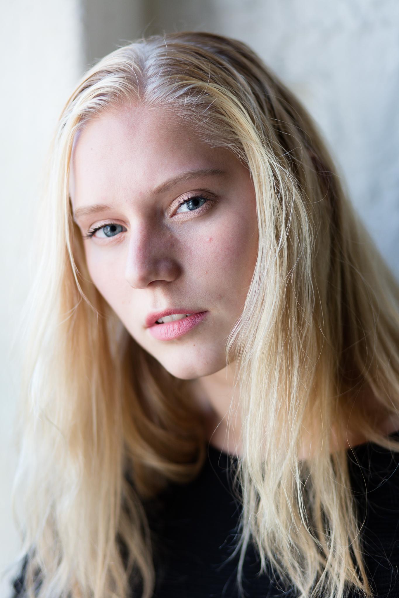 Natuurlijk portret van een jonge vrouw met blond haar en blauwe ogen bij raamlicht