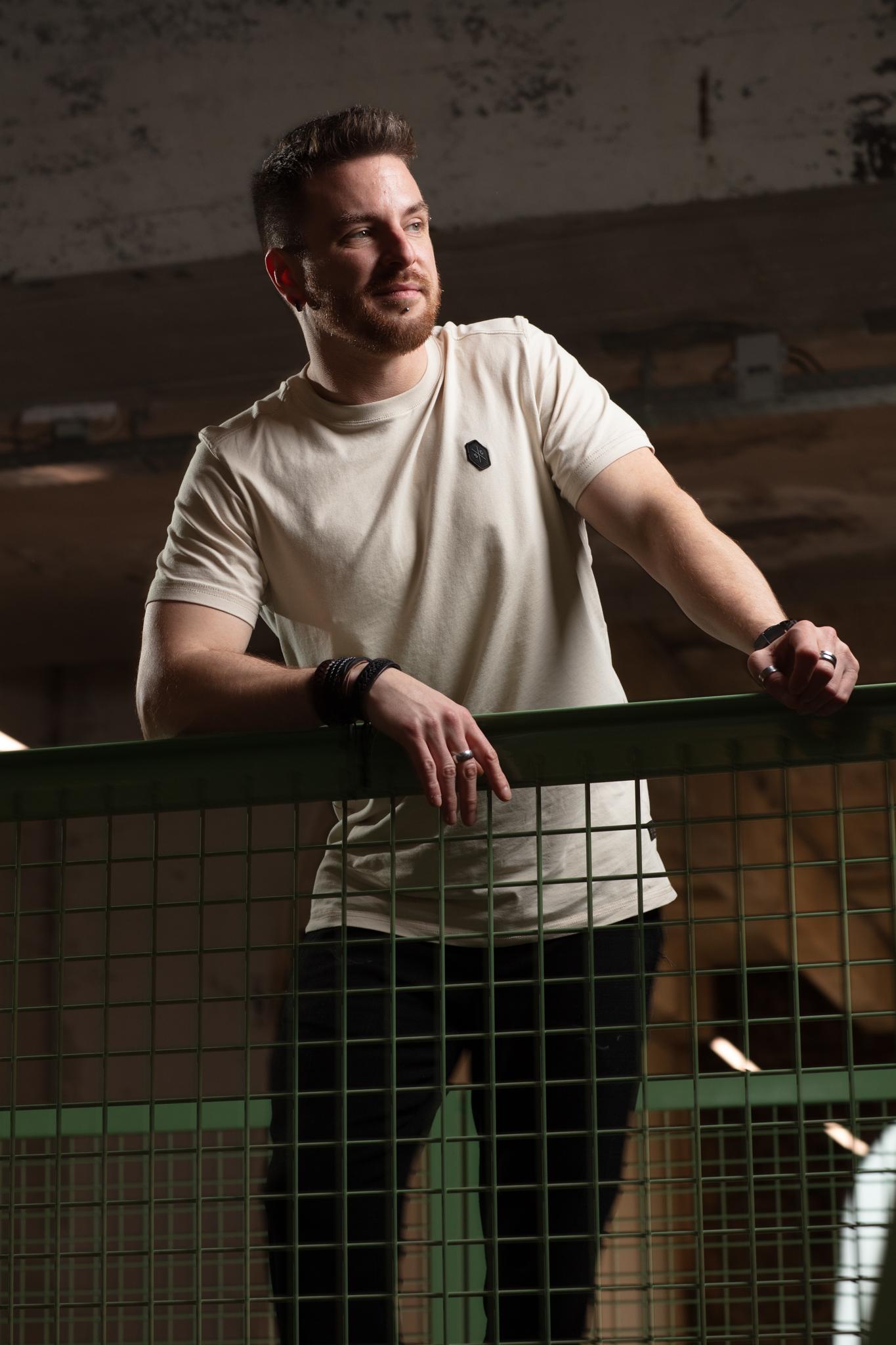 Stoer mannenportret van een man leunend op een metalen hek in industriële omgeving